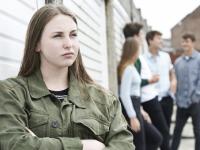 Ung pige ser utilfreds og tænksom ud, mens fire andre står og snakker bag hende
