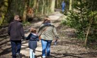 En mor og far går hånd i hånd med deres datter ude i en skov med ryggen til.